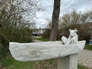 Ein kunstvoll gestaltetes Boot aus Stein mit einer kleinen Tierfigur als Blickfang im Grünen.