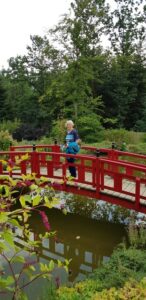 Eine Teilnehmerin posiert lächelnd auf einer rot lackierten Holzbrücke über einem Teich.