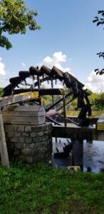 Ein altes hölzernes Wasserrad thront über dem ruhig fließenden Flusswasser.