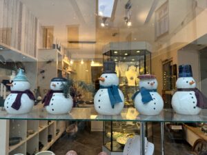 Fünf getöpferte Schneemänner mit Filzschals begrüßen die Passanten im Schaufenster.
