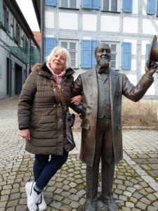 Lächelnd stellt sich eine Teilnehmerin neben die Bronzestatue eines Herrn mit Hut.