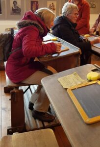 Auf alten Schulbänken probieren die Teilnehmerinnen das Schreiben mit Schiefertafeln.