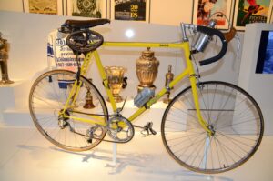 Ein gelbes Rennrad mit Pokalen und Erinnerungsstücken aus dem Radsport