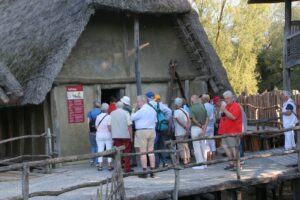 Pfahlbaumuseum: Reisegruppe vor strohgedeckter Steinzeithütte