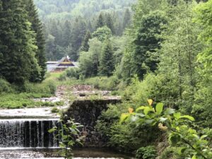 Kleiner Kaskadenwasserfall mit Bauden-Dach im Hintergrund