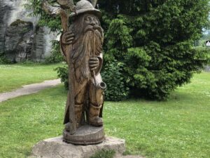 Geschnitzte Berggeist-Figur mit Hut und Wanderstab im Park