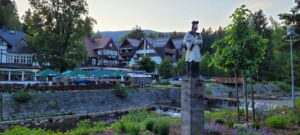 Steinerne Figur auf Sockel vor traditioneller Bauden-Architektur