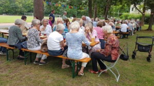 Gäste an einer Tischreihe mit Blick auf den Sportplatz