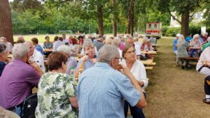 Gäste an Tischreihen unter Bäumen